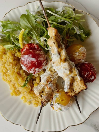 "Chicken skewers served with a side of lentils, garnished with sauce and salad