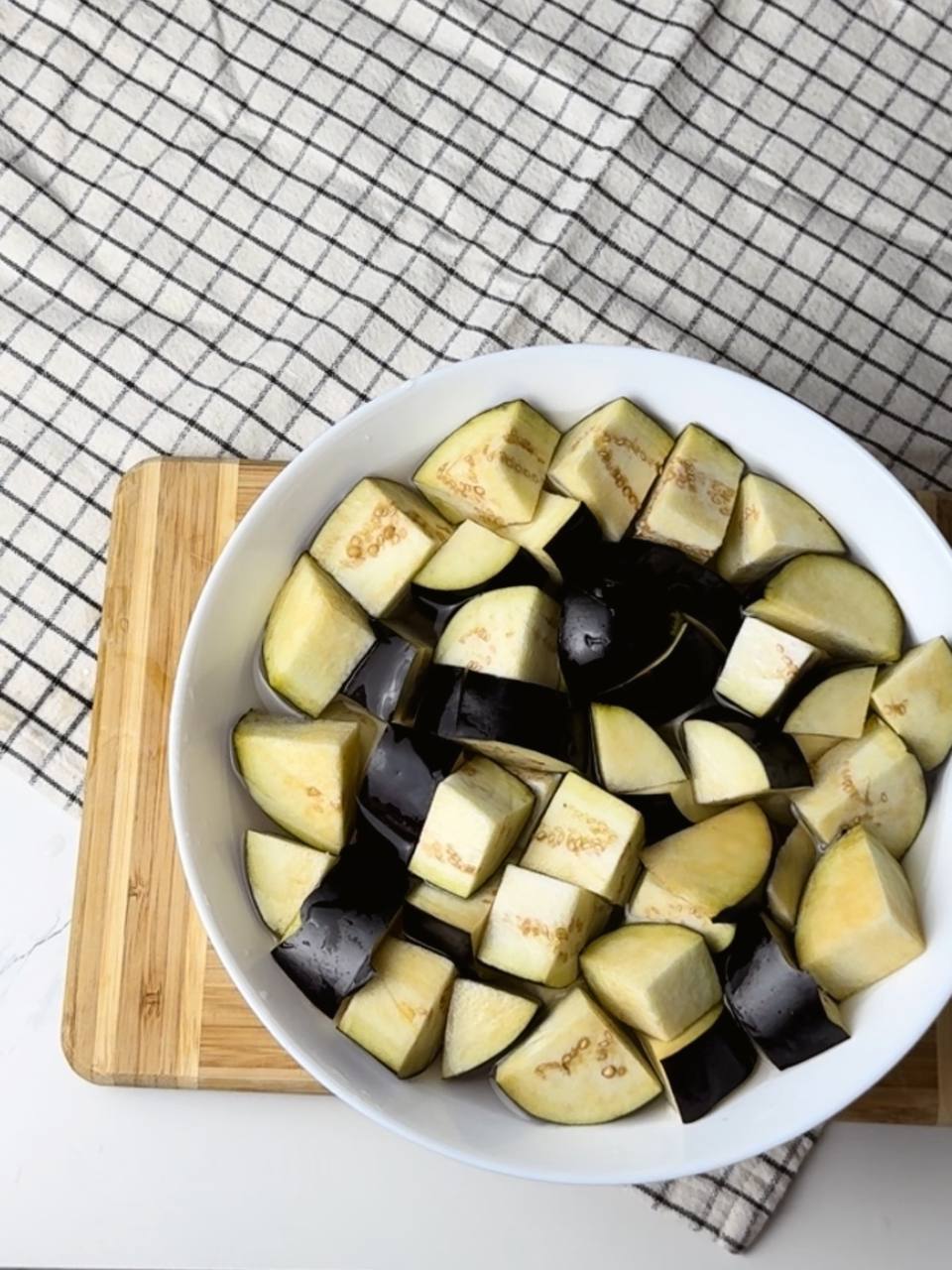 Large chunks of eggplant on a cutting board, ready to be soaked and fried for the salad.