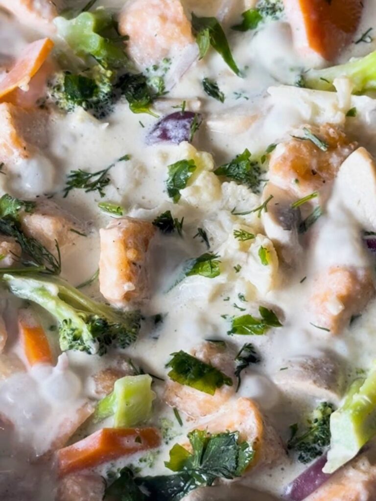 Rich, creamy garlic sauce poured over seared salmon and vegetables in a pan.
