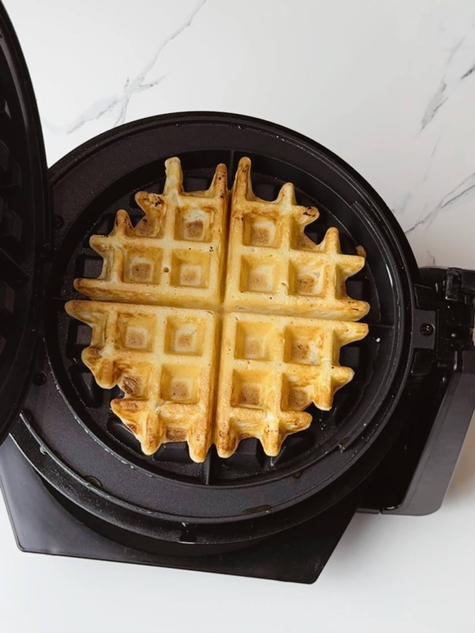A freshly baked golden Belgian waffle inside a waffle iron, crispy on the outside and soft inside.