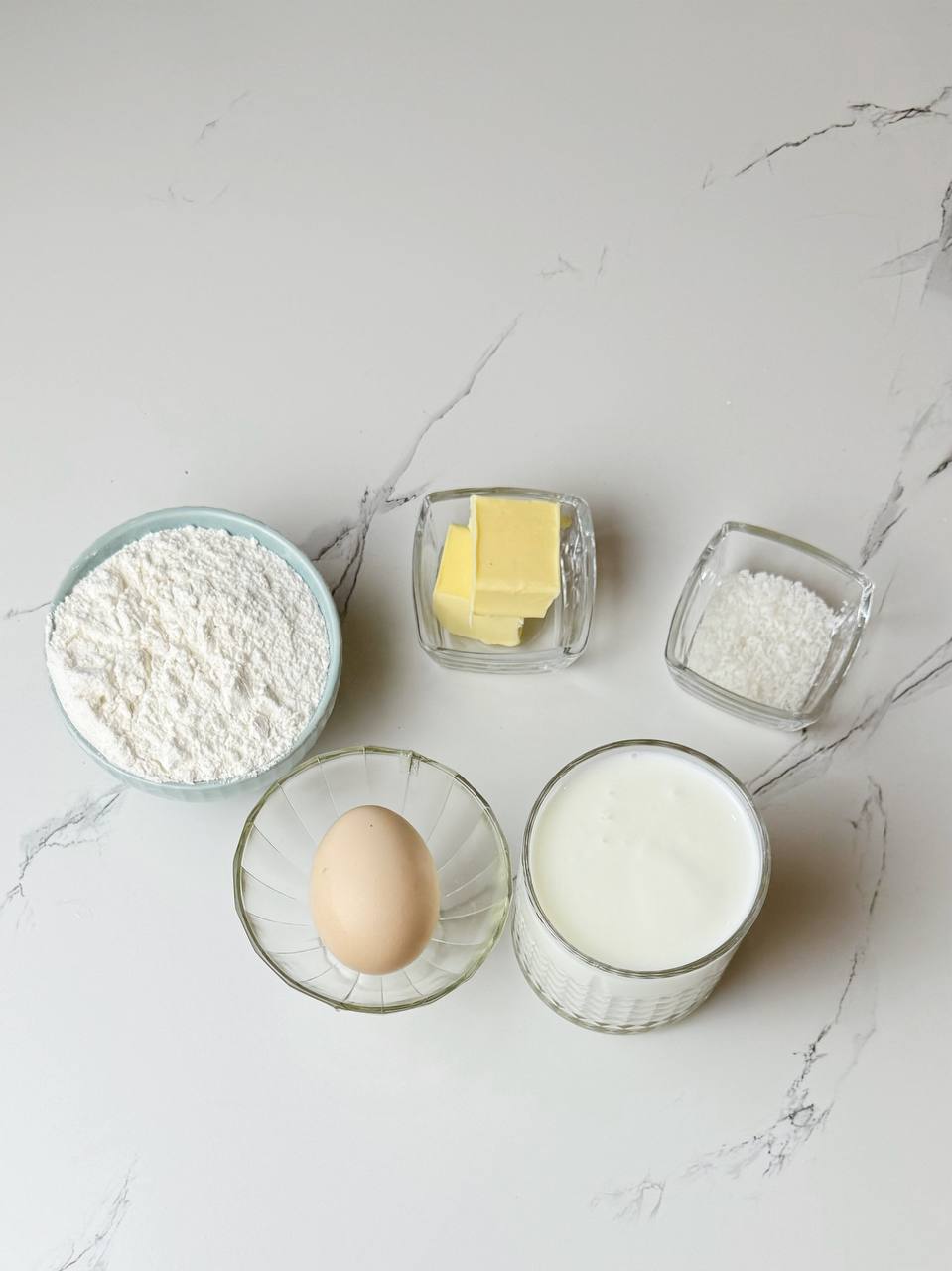 Ingredients for crispy Belgian waffles, including eggs, flour, sugar, milk, and butter, neatly arranged on a countertop.