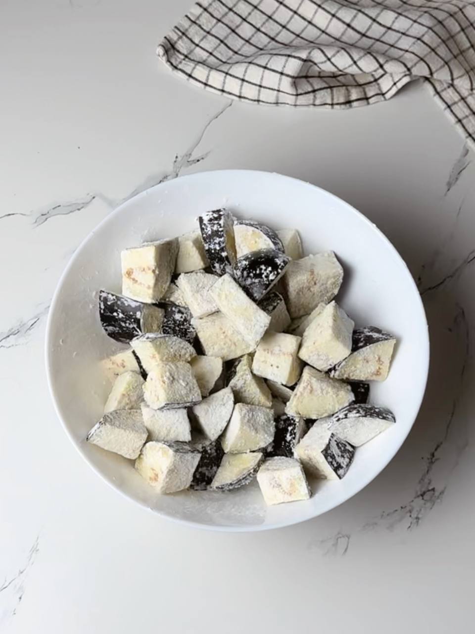 Eggplant chunks coated in cornstarch, ready to be fried to crispy perfection.