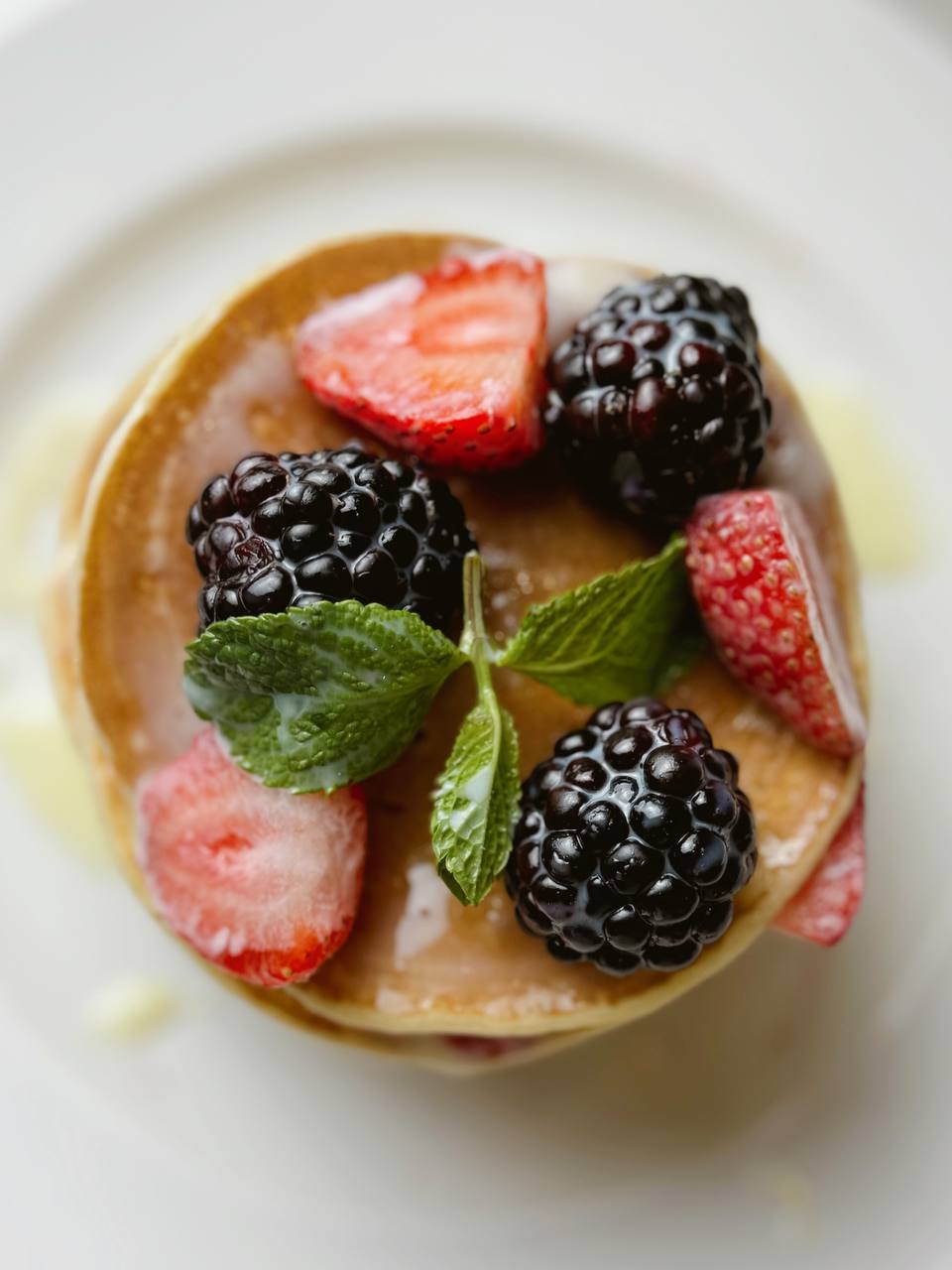 A plate of pancakes topped with fresh berries and mint
