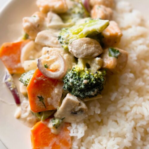 A plate of creamy garlic salmon with vegetables, served over rice and garnished with fresh parsley.
