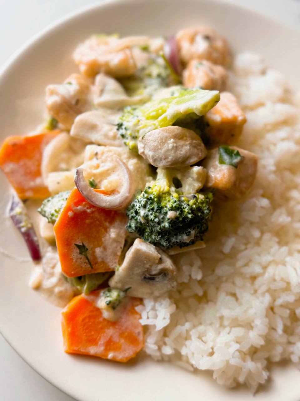 A plate of creamy garlic salmon with vegetables, served over rice and garnished with fresh parsley.