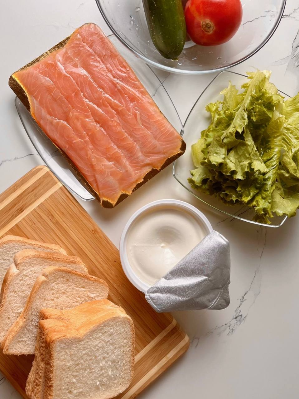Ingredients for a salmon club sandwich on a wooden board.