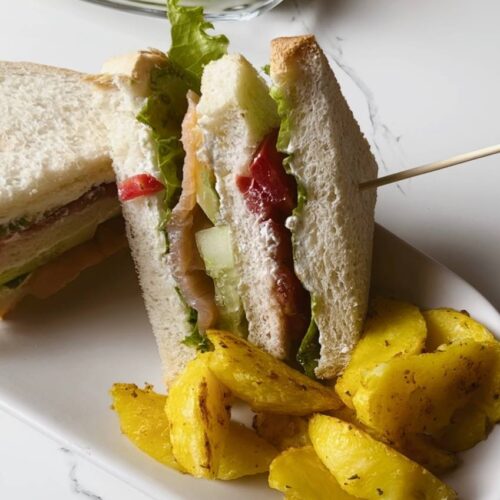 A plated salmon club sandwich with a side of potato wedges