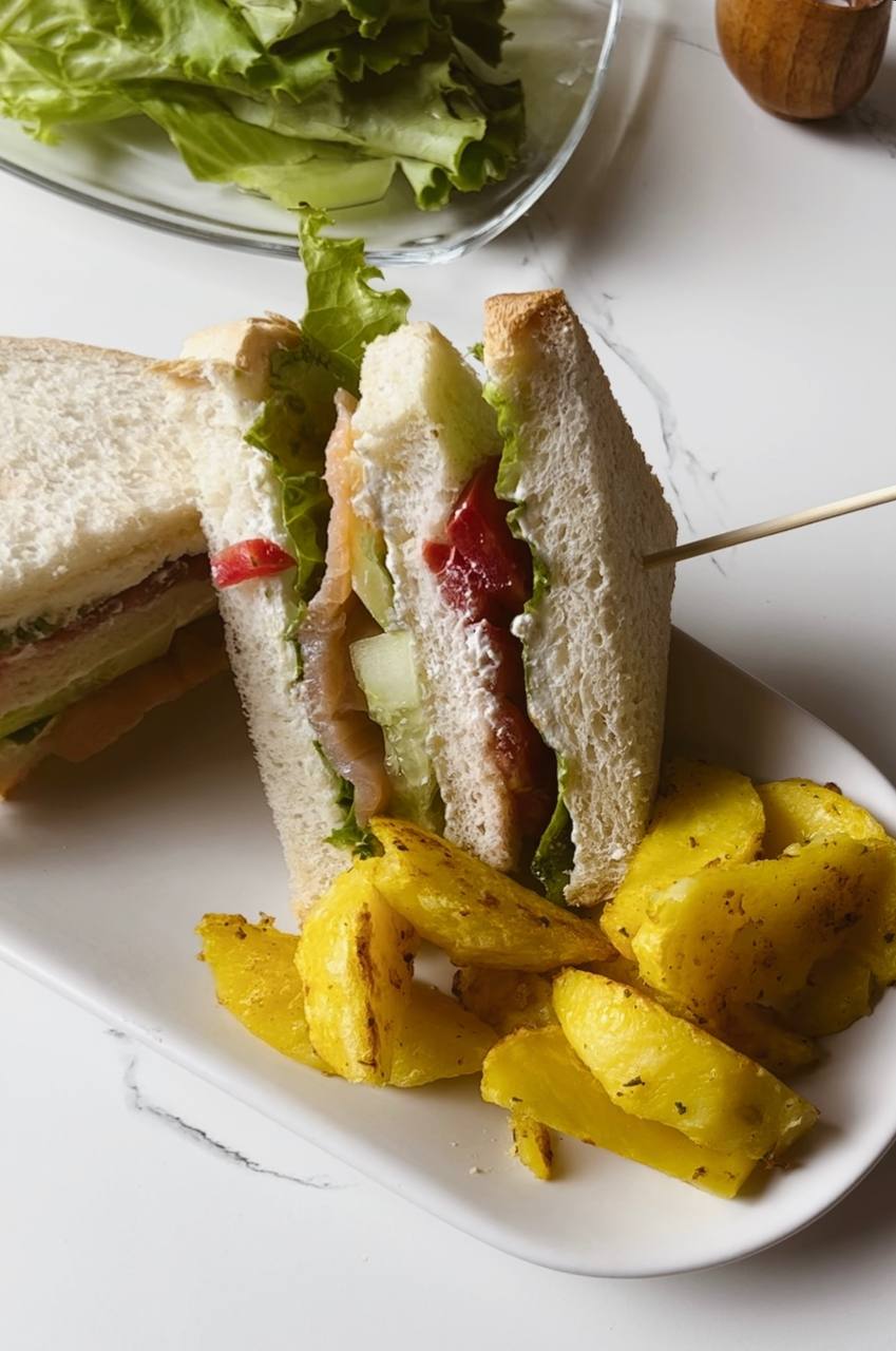 A plated salmon club sandwich with a side of potato wedges