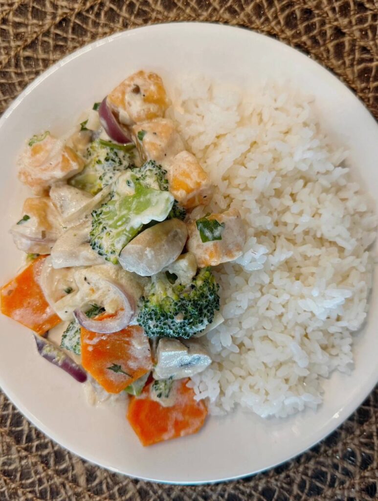A close-up of creamy garlic salmon with vegetables, served with rice and fresh herbs.
