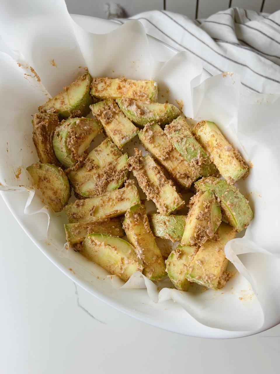 Zucchini sticks coated in breadcrumbs, parmesan, and spices, arranged on a baking sheet.