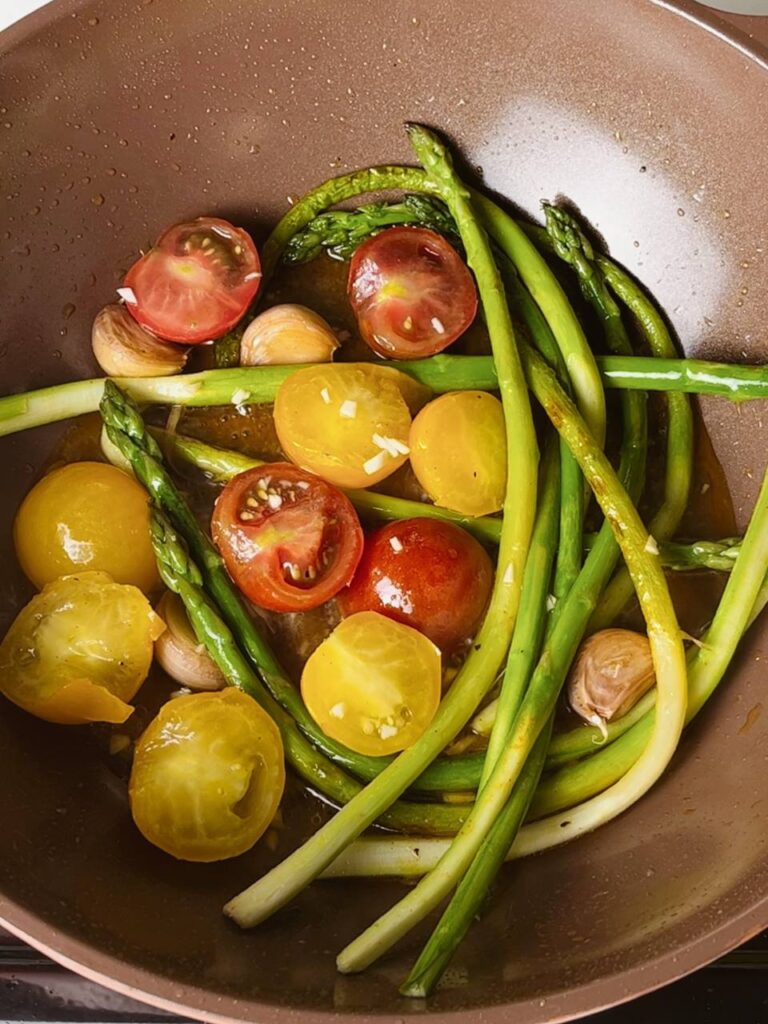 Asparagus in a pan with cherry tomatoes and garlic for a flavorful side.