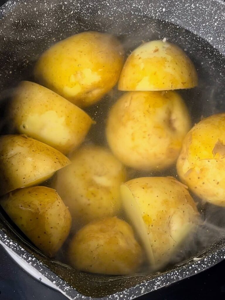 Halved potatoes boiling in a pot of water for roasting.
