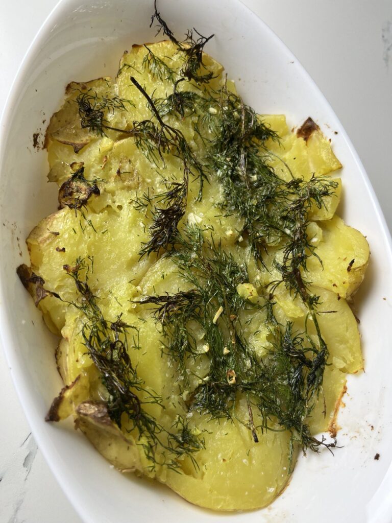 Golden roasted potatoes on a baking sheet drizzled with garlic herb sauce.