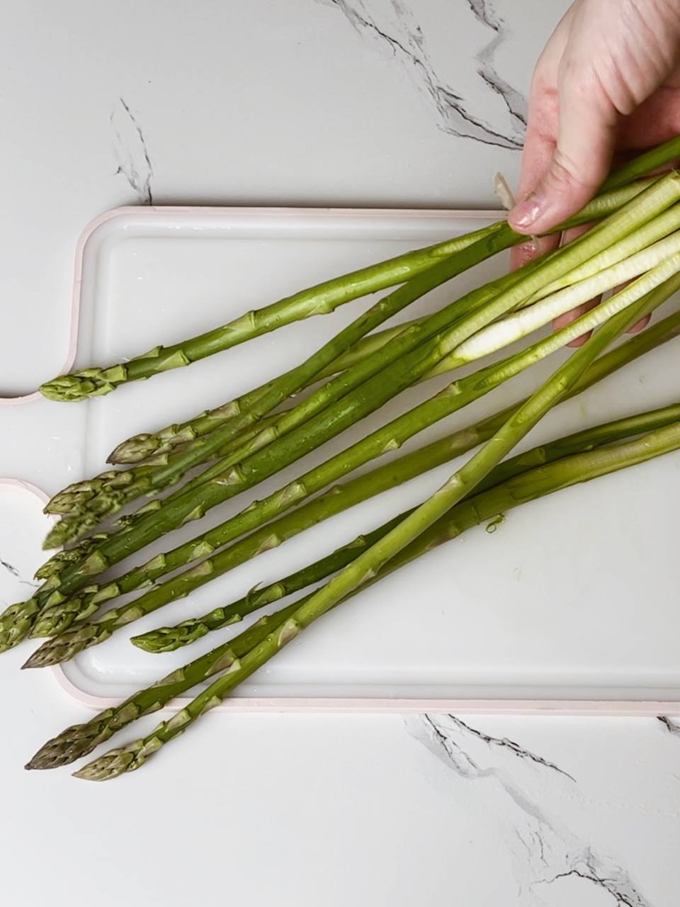 Fresh asparagus with trimmed ends on a wooden cutting board, ready for cooking.