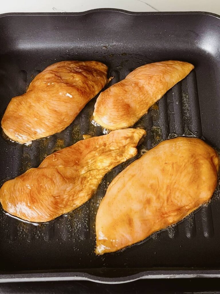 Marinated chicken breast cooking on a grill pan with golden grill marks.