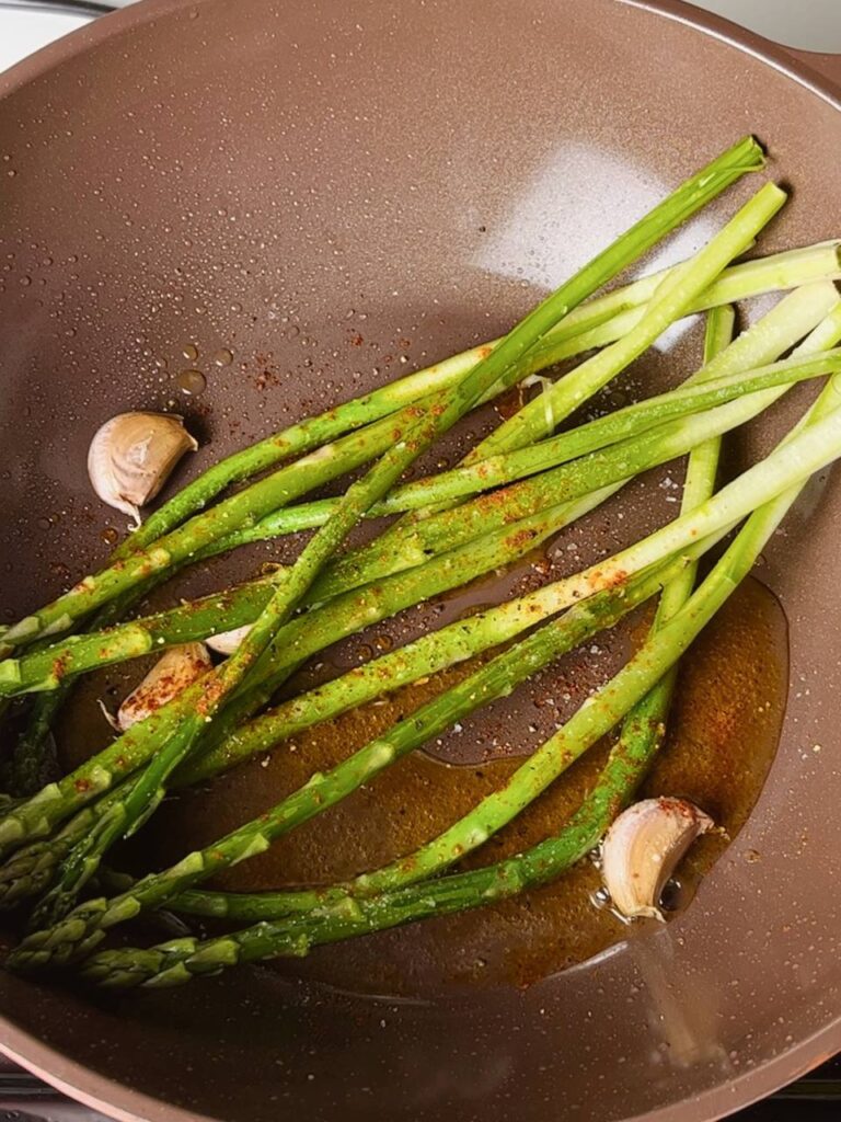 Fresh asparagus cooking in a pan with garlic and seasonings.