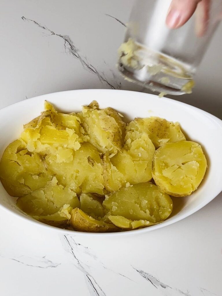 Pressing boiled potatoes with a glass on a baking sheet before roasting.