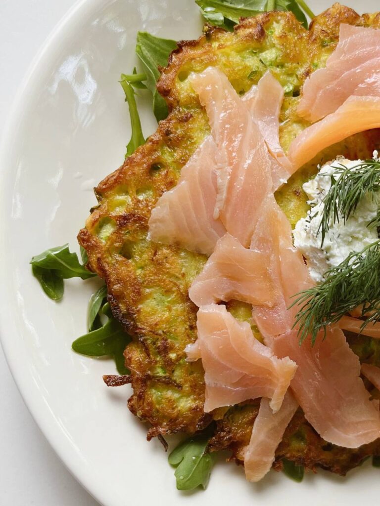 A close-up of a potato zucchini pancake with creamy garlic topping and smoked salmon