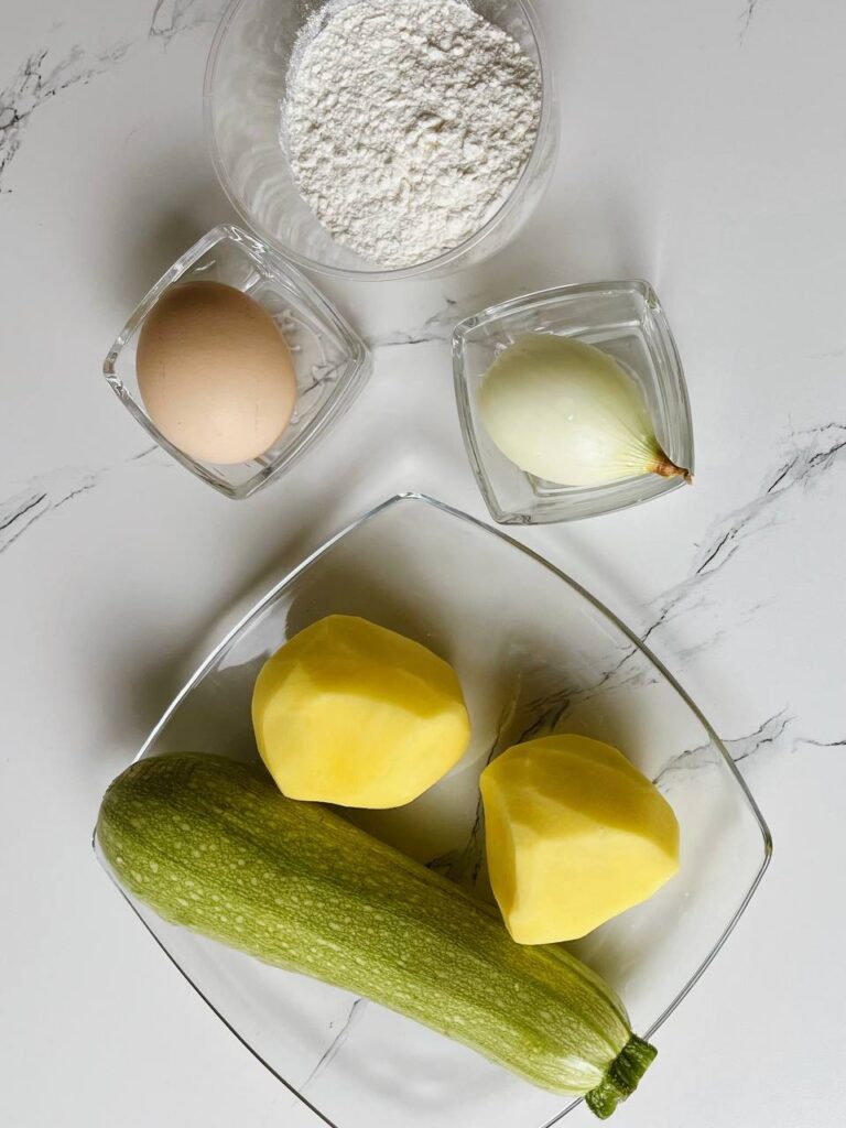 Ingredients for potato zucchini pancakes, including potatoes, zucchini, egg, onion, and flour.