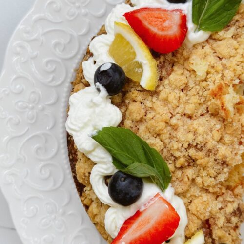 Close-up of lemon yogurt cake topped with whipped cream, berries, and mint