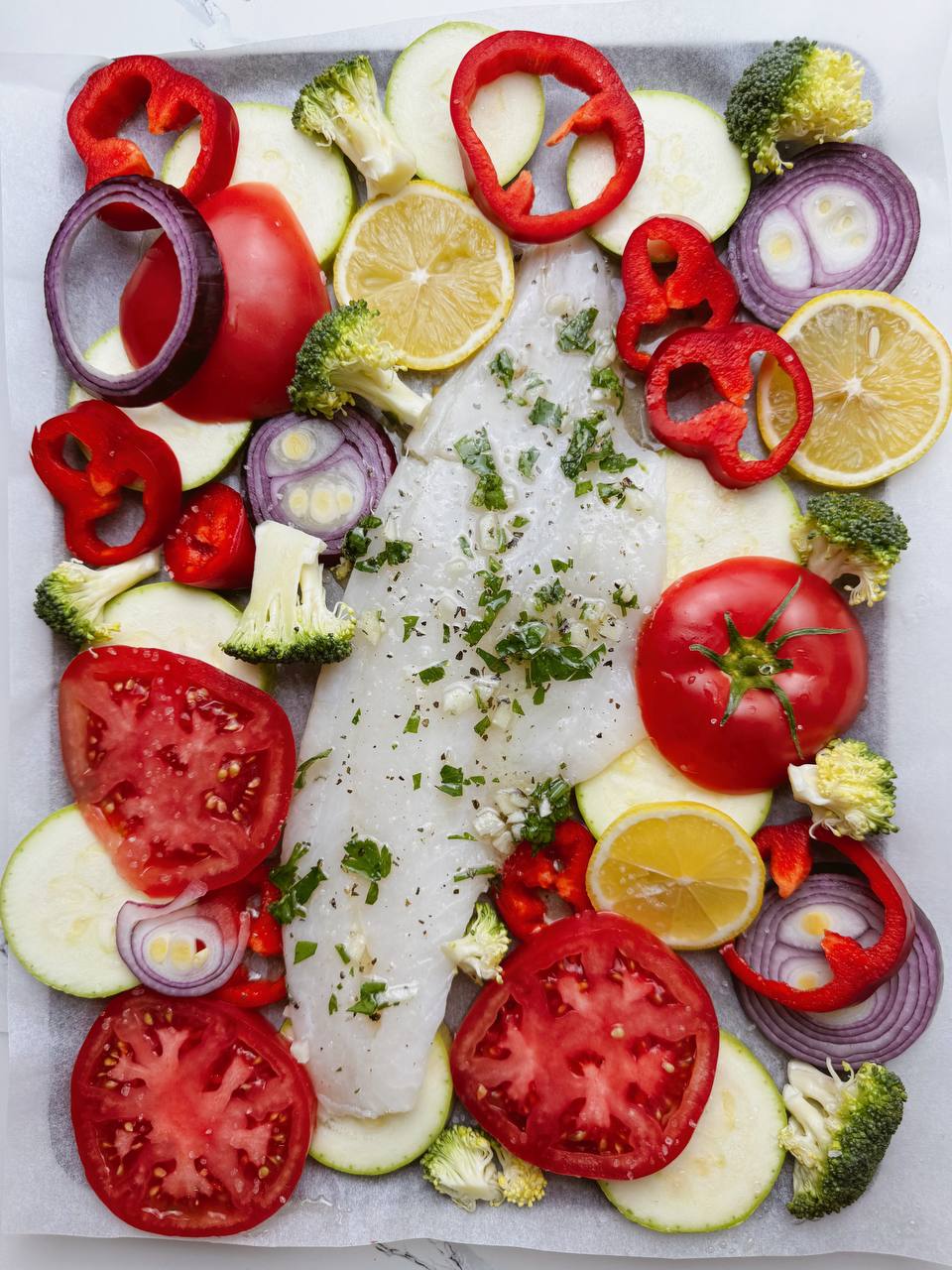 Cod fillets layered on fresh vegetables, ready to bake