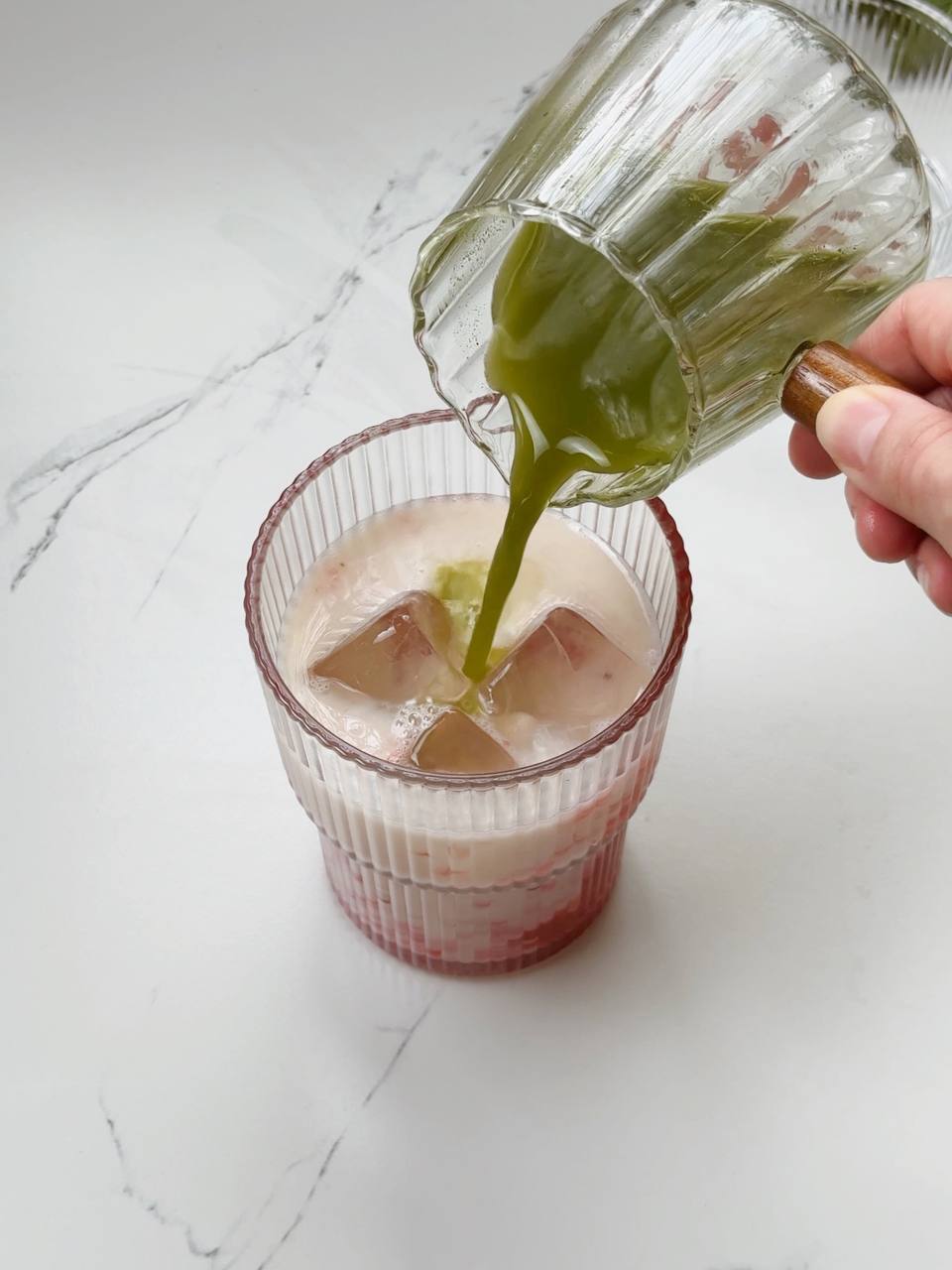 Pouring matcha over ice, milk, and strawberry puree for layered iced latte