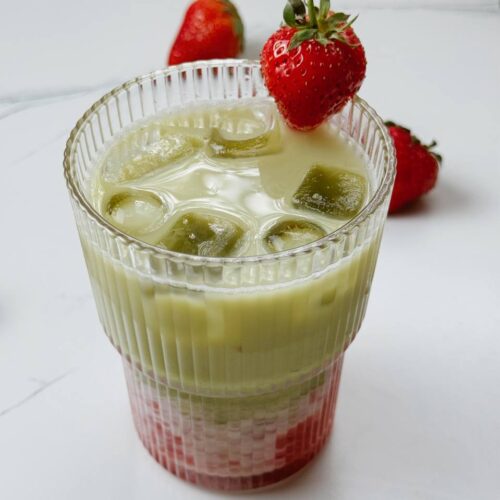 Strawberry iced matcha latte in a glass, topped with fresh strawberry and layered colors