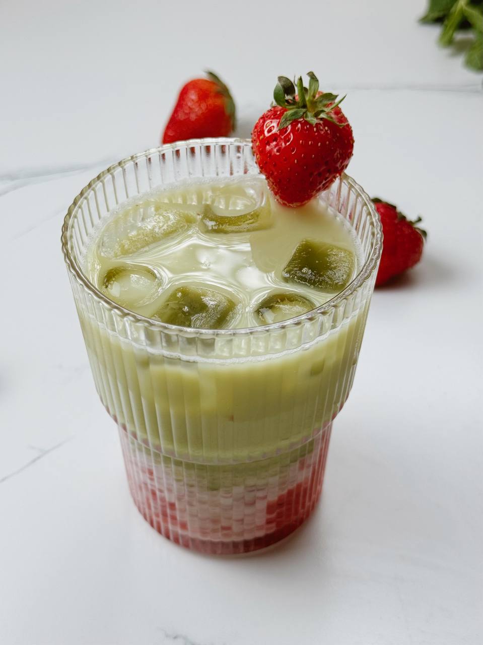 Strawberry iced matcha latte in a glass, topped with fresh strawberry and layered colors