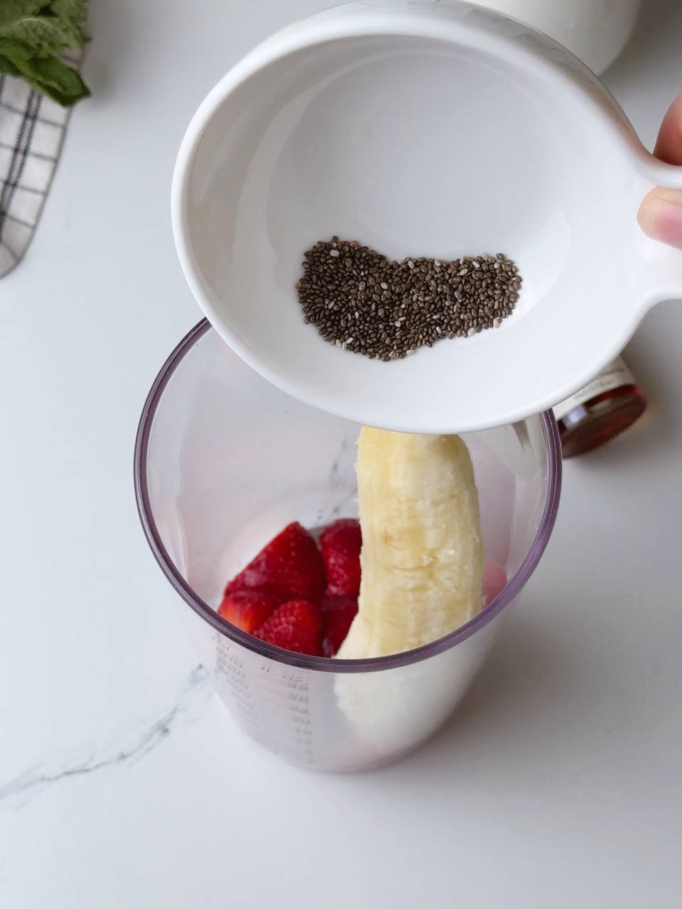Adding chia seeds to blender cup with banana and strawberry for healthy milkshake.