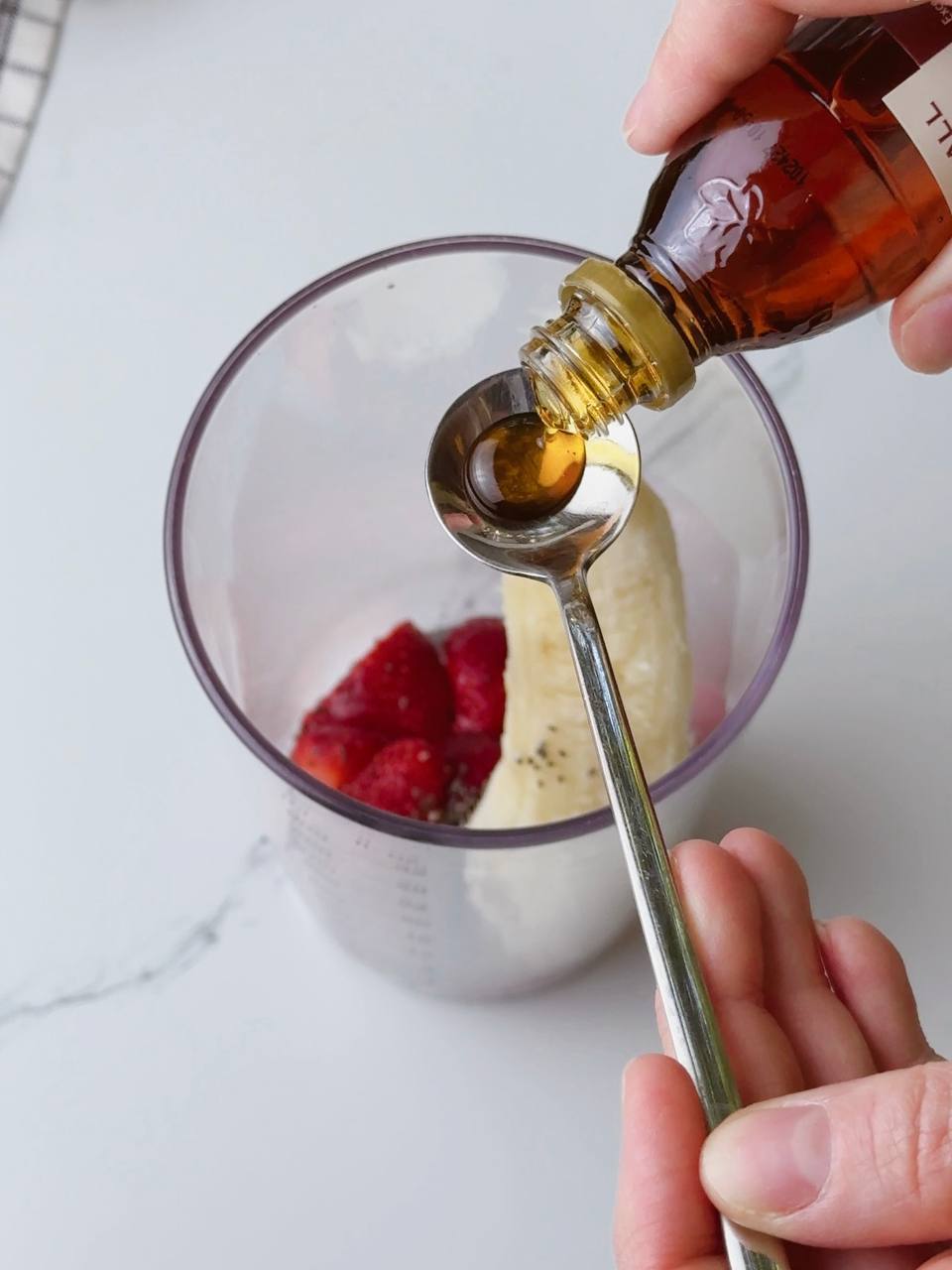 Drizzling maple syrup with spoon into milkshake blender for natural sweetness