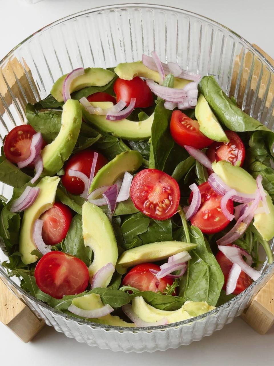 Assembling salad with greens, tomatoes, avocado, and vinaigrette in a large bowl