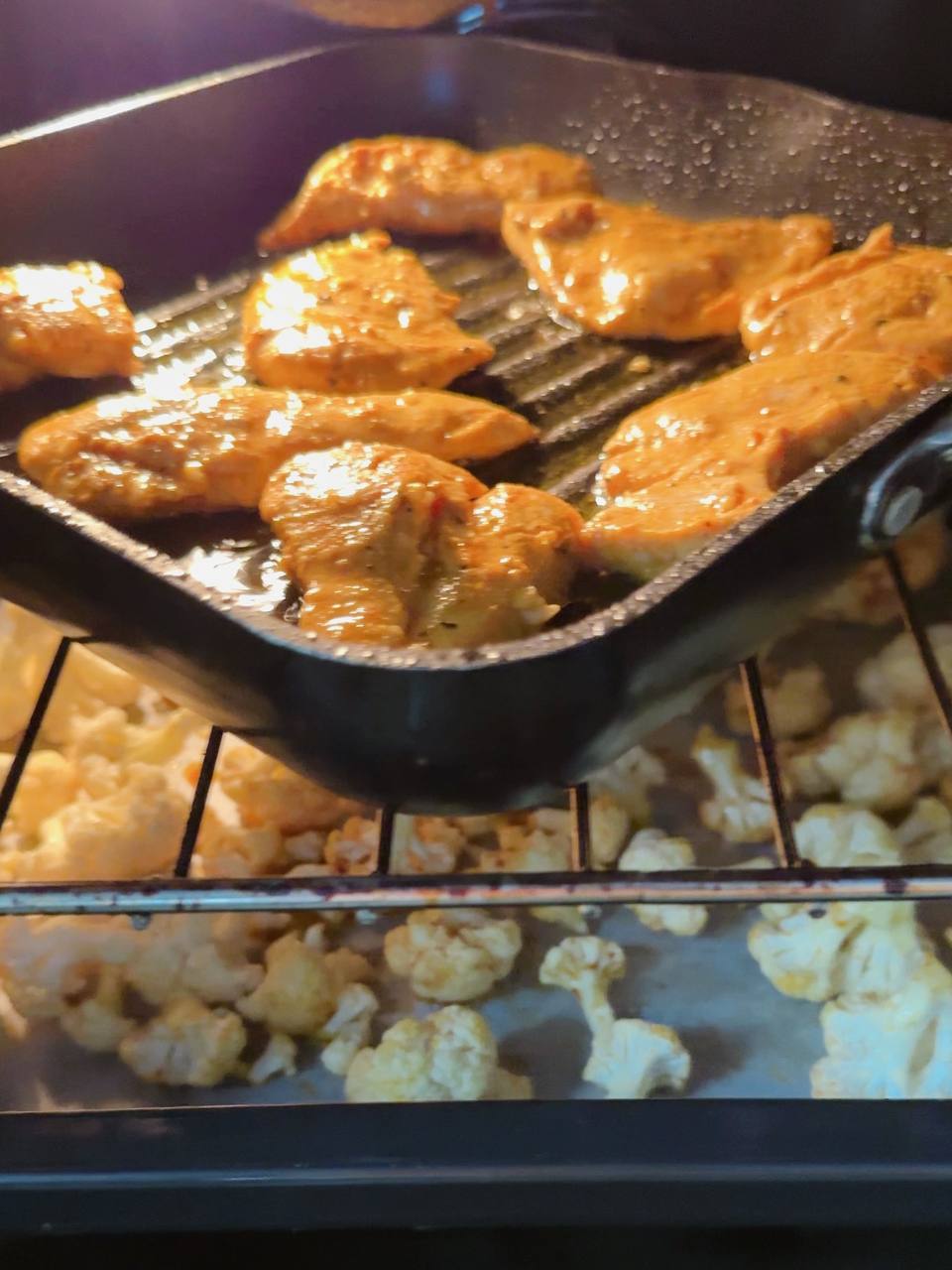 Chicken cooking on a grill pan while cauliflower roasts in the oven