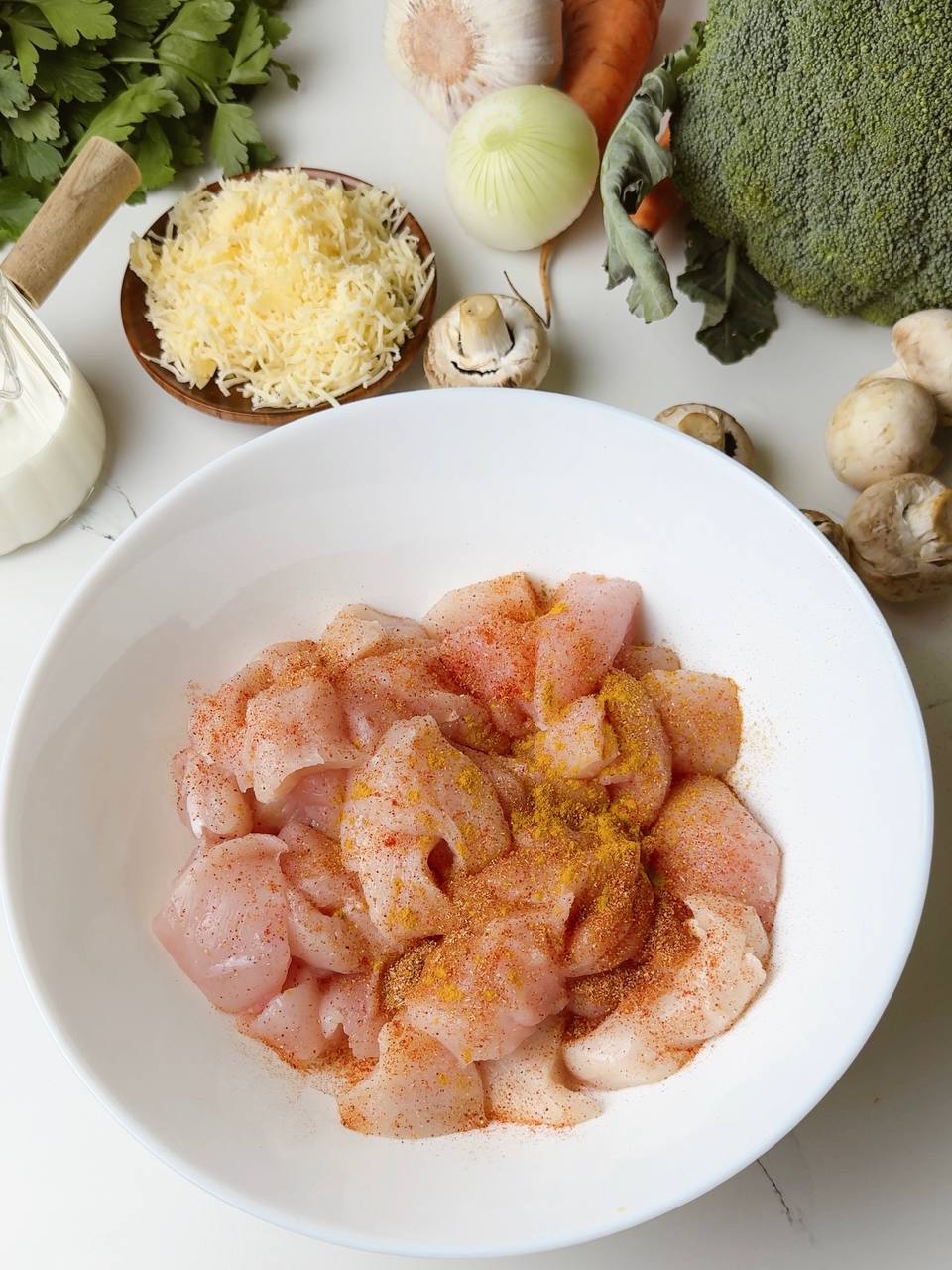 Chicken pieces with spices in a white bowl before cooking