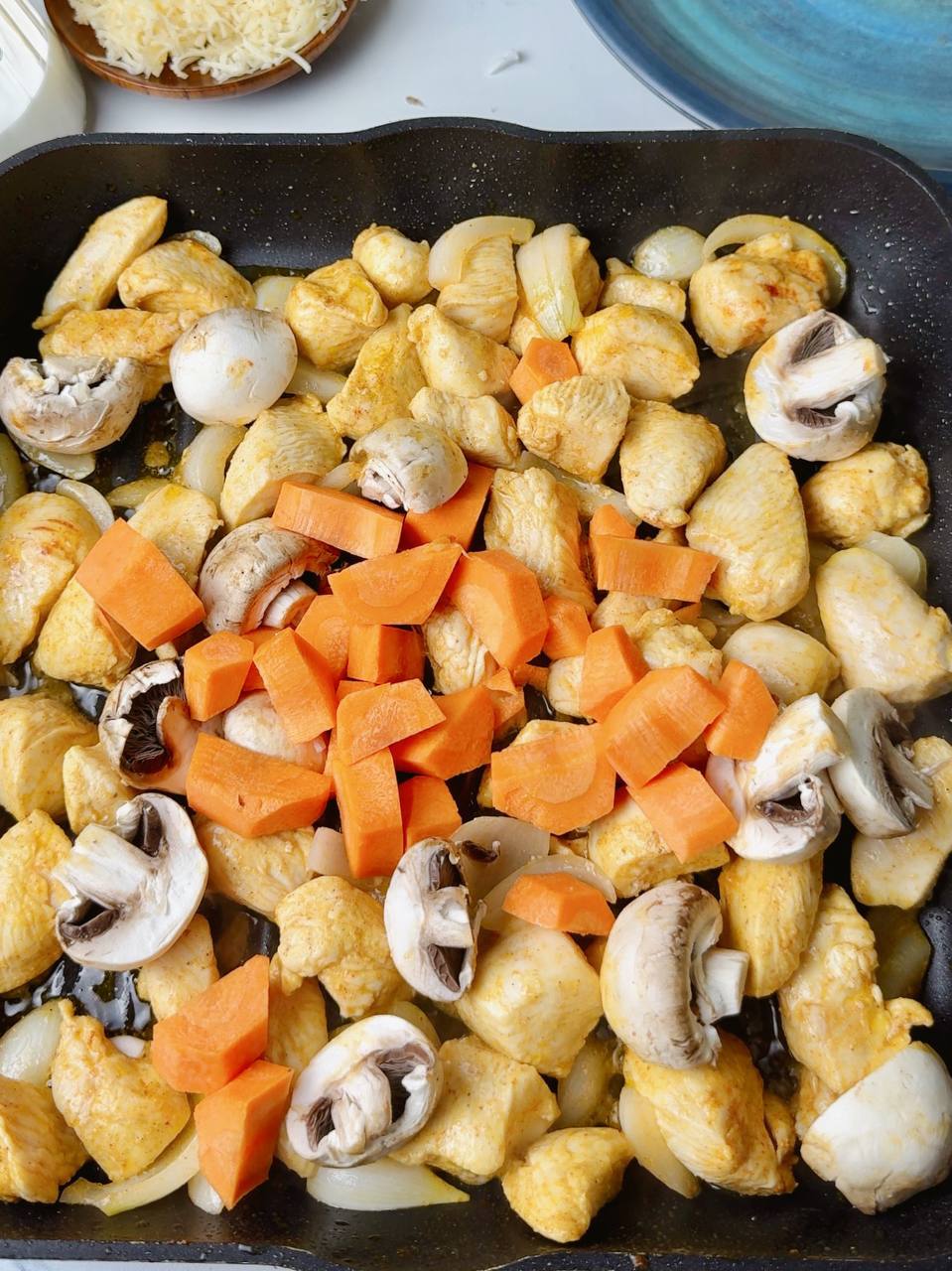 Chicken with carrots, mushrooms, and onion sautéing in a pan