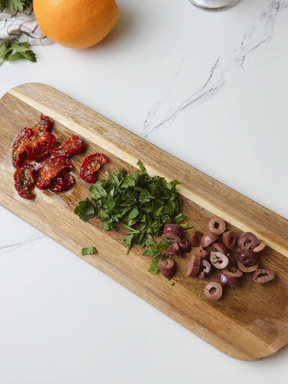 Chopped parsley, olives, and sun-dried tomatoes on a wooden board ready to add to baked potatoes