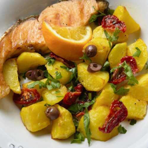 Close view of baked salmon with golden potatoes, sun-dried tomatoes, parsley, and a lemon wedge
