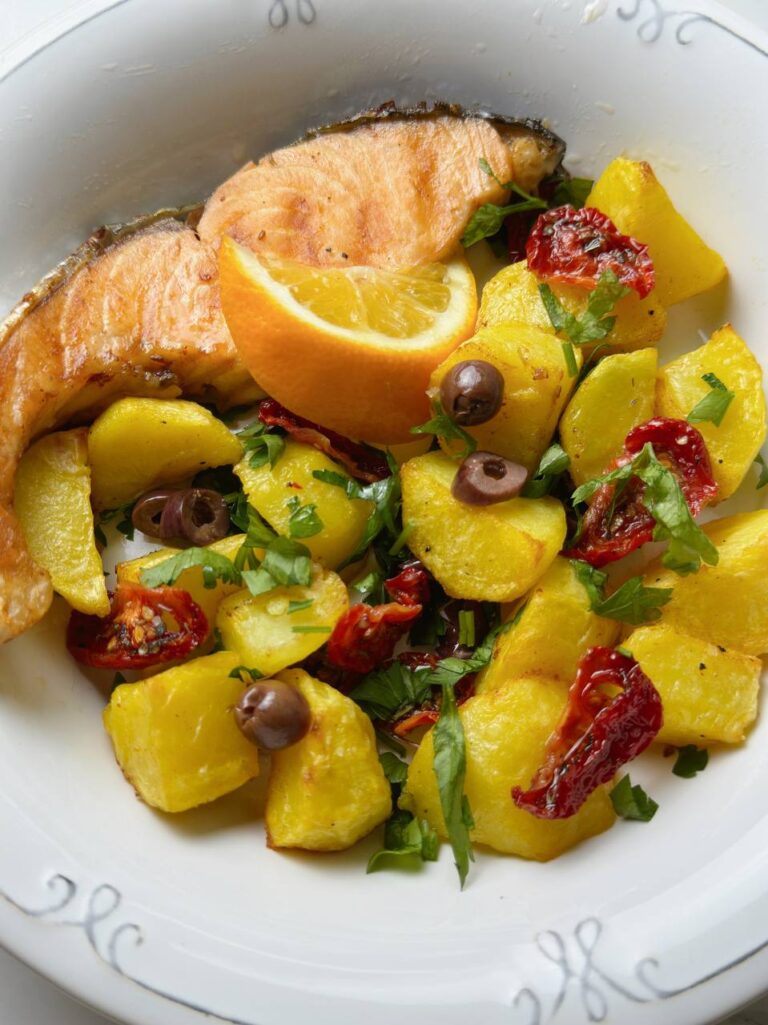 Close view of baked salmon with golden potatoes, sun-dried tomatoes, parsley, and a lemon wedge
