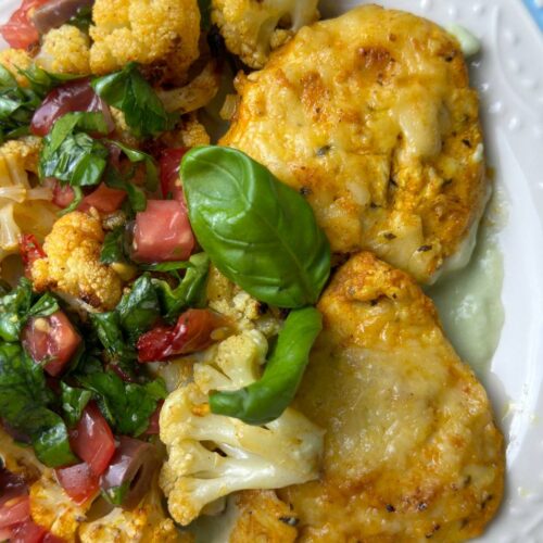 Close-up view of served yogurt chicken with avocado sauce and roasted cauliflower