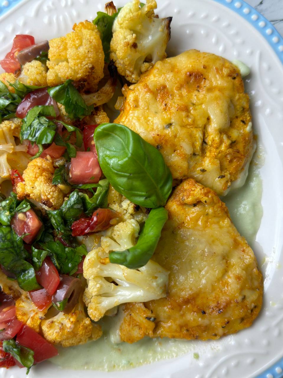 Close-up view of served yogurt chicken with avocado sauce and roasted cauliflower