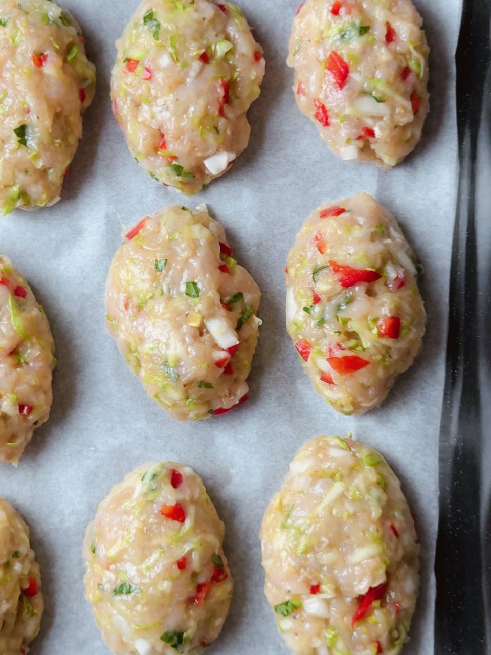 Shaped chicken and zucchini fritters on a baking tray before baking