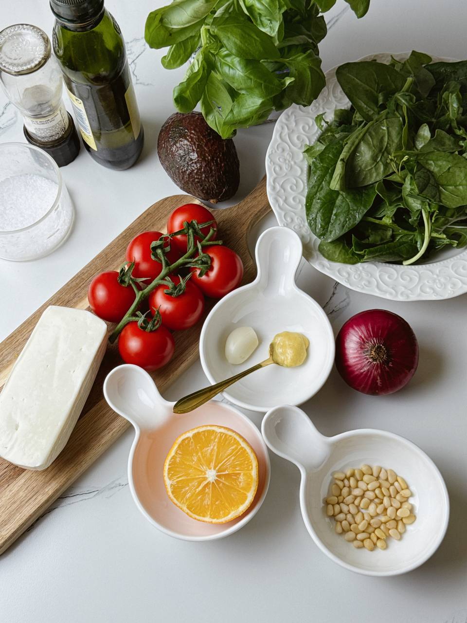 Fresh ingredients for grilled halloumi salad including halloumi cheese, cherry tomatoes, avocado, arugula, red onion, and basil