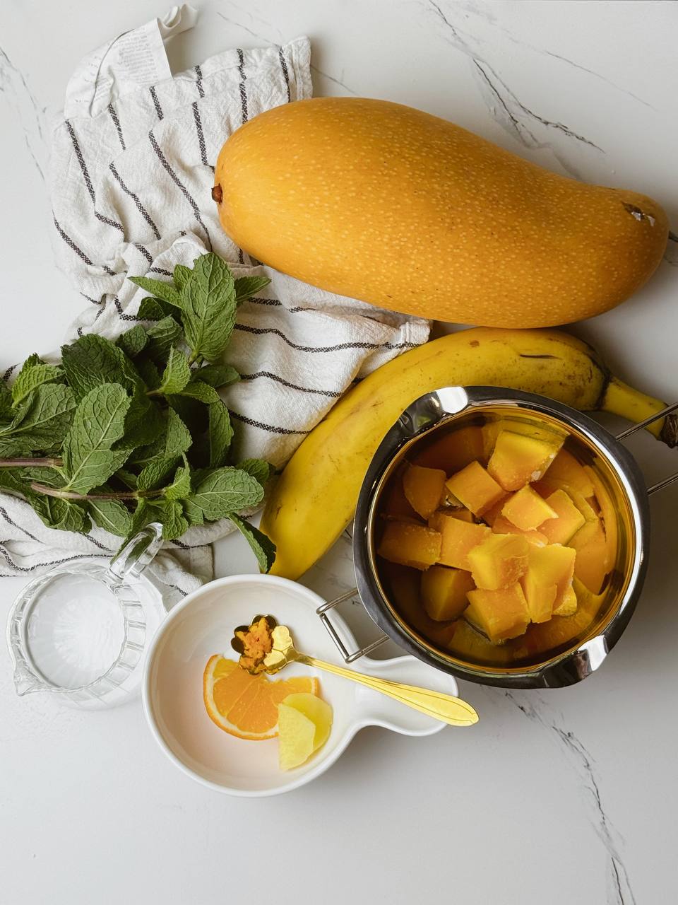 All ingredients for Mango Banana Ginger Smoothie including banana, mango, ginger, lemon, and orange peel