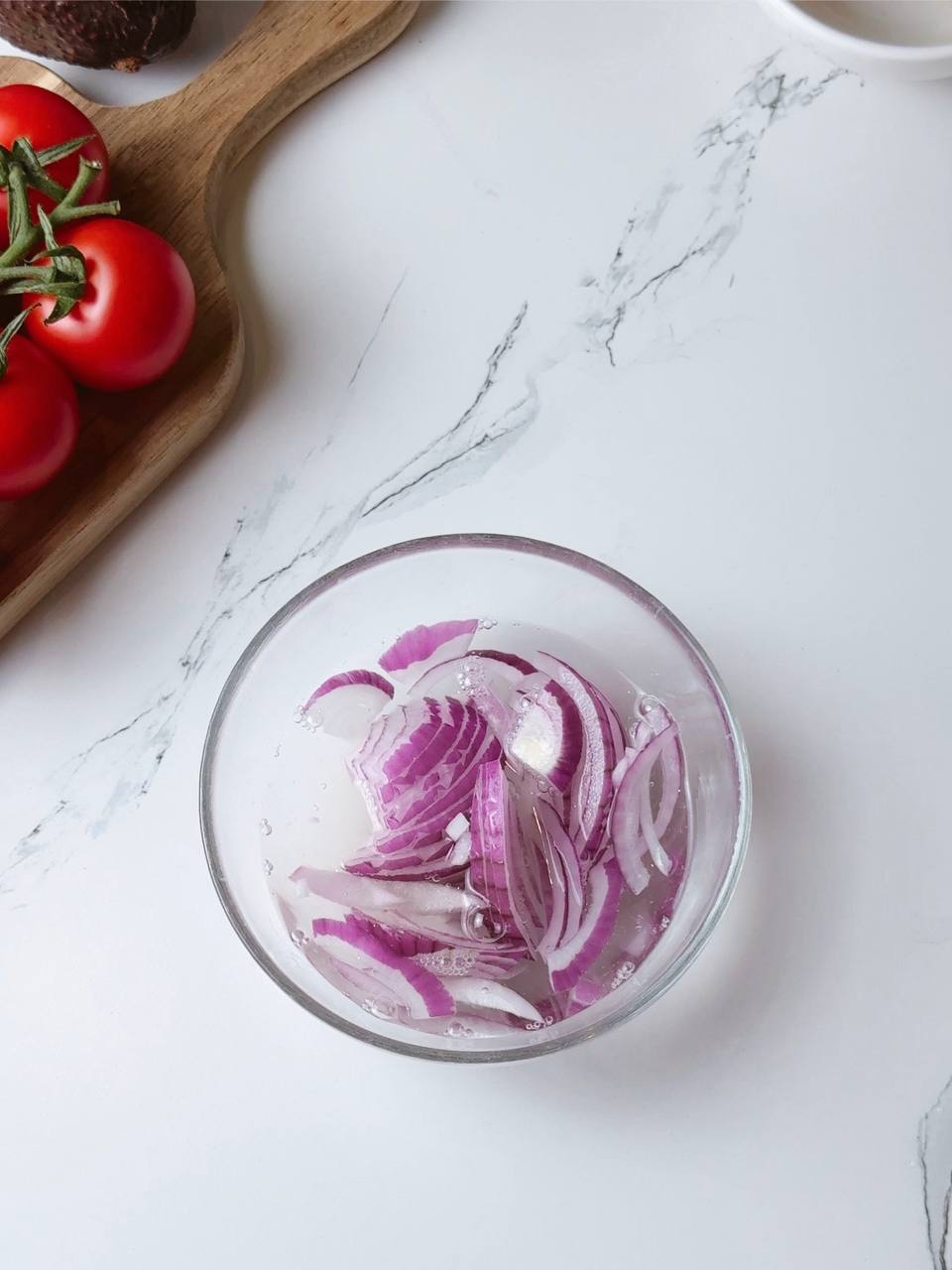 Sliced red onion marinating in lemon juice, honey, and hot water in a glass bowl
