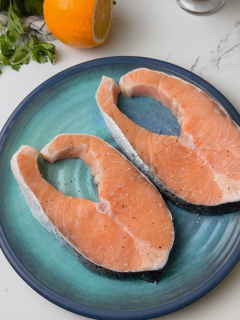 Raw salmon steaks on a plate seasoned with salt, pepper, and lemon juice