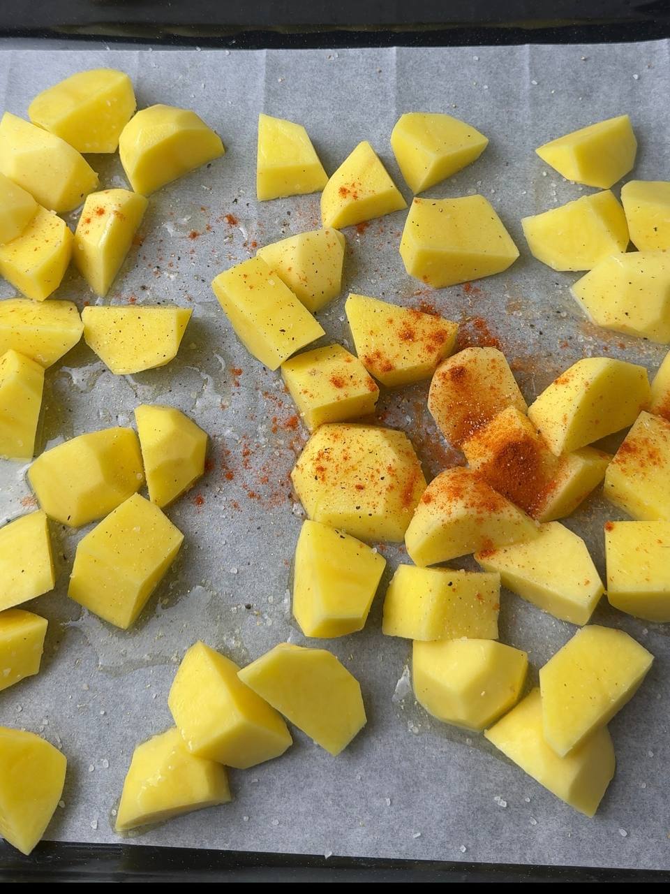 Cut baby potatoes on a baking tray with olive oil and spices ready for roasting