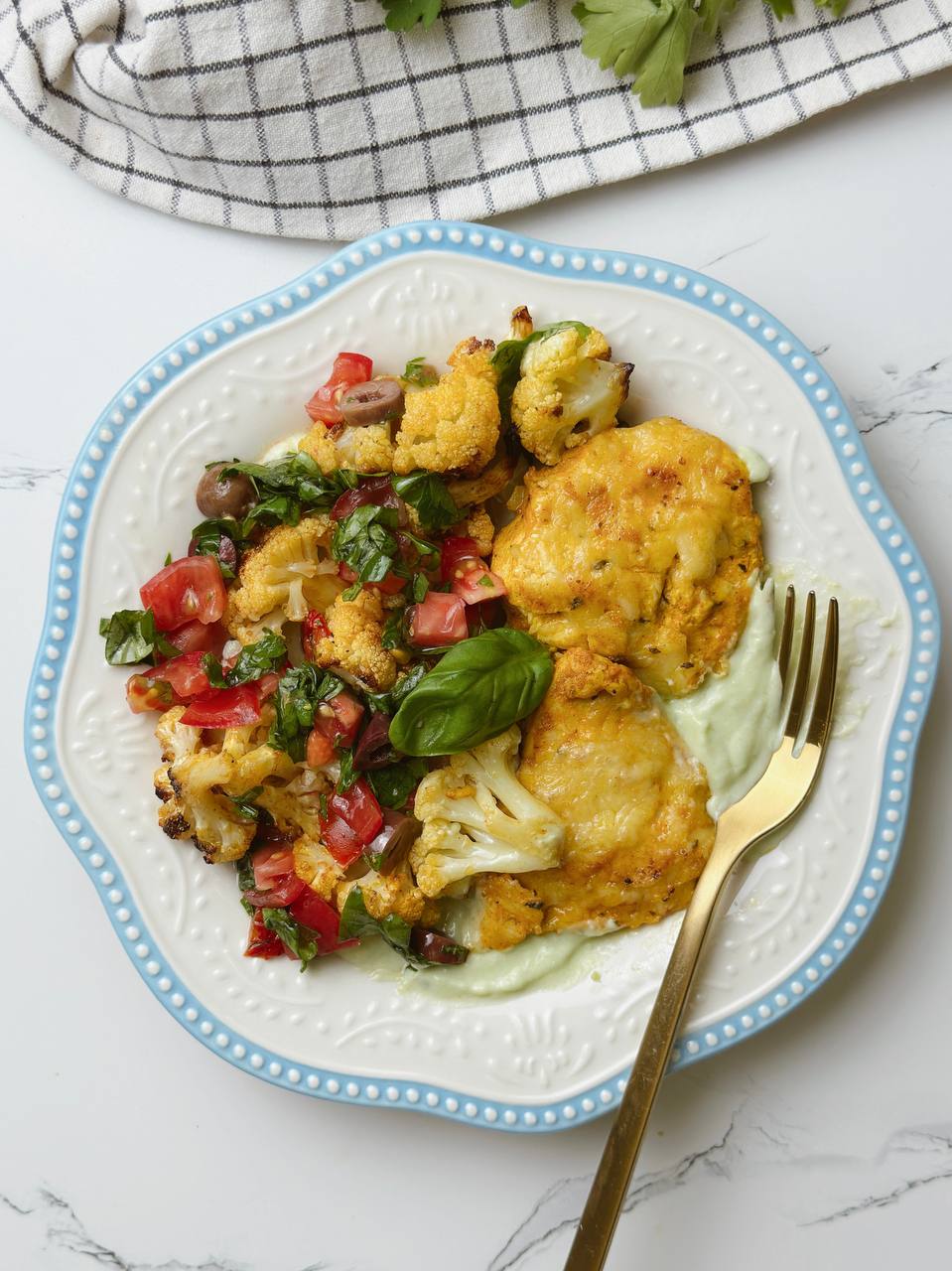 Plate of yogurt chicken with avocado sauce and roasted cauliflower, served with a fork ready to eat