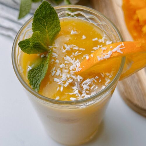 Close-up of Mango Banana Ginger Smoothie with coconut sprinkles, mint, and lemon slice