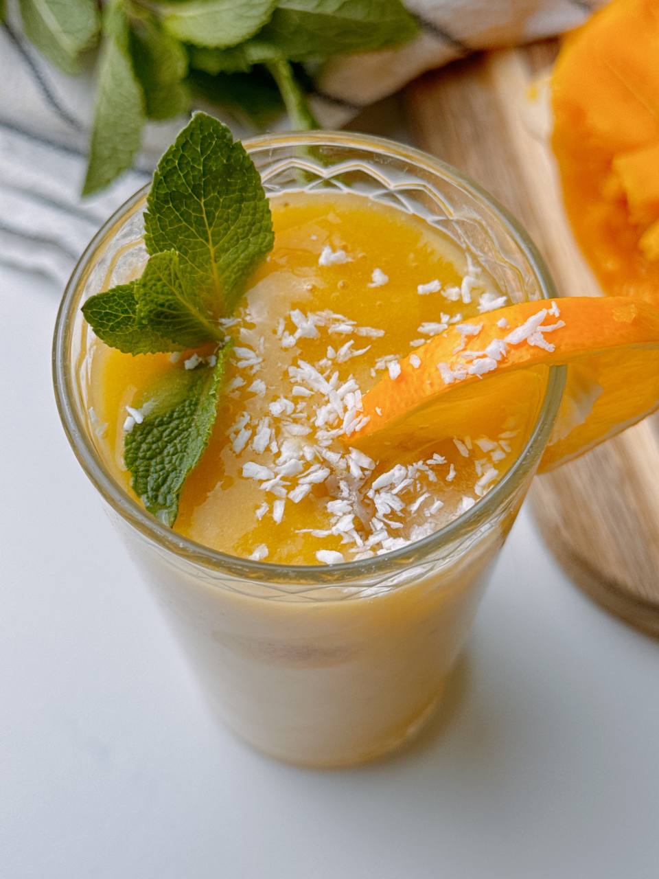 Close-up of Mango Banana Ginger Smoothie with coconut sprinkles, mint, and lemon slice