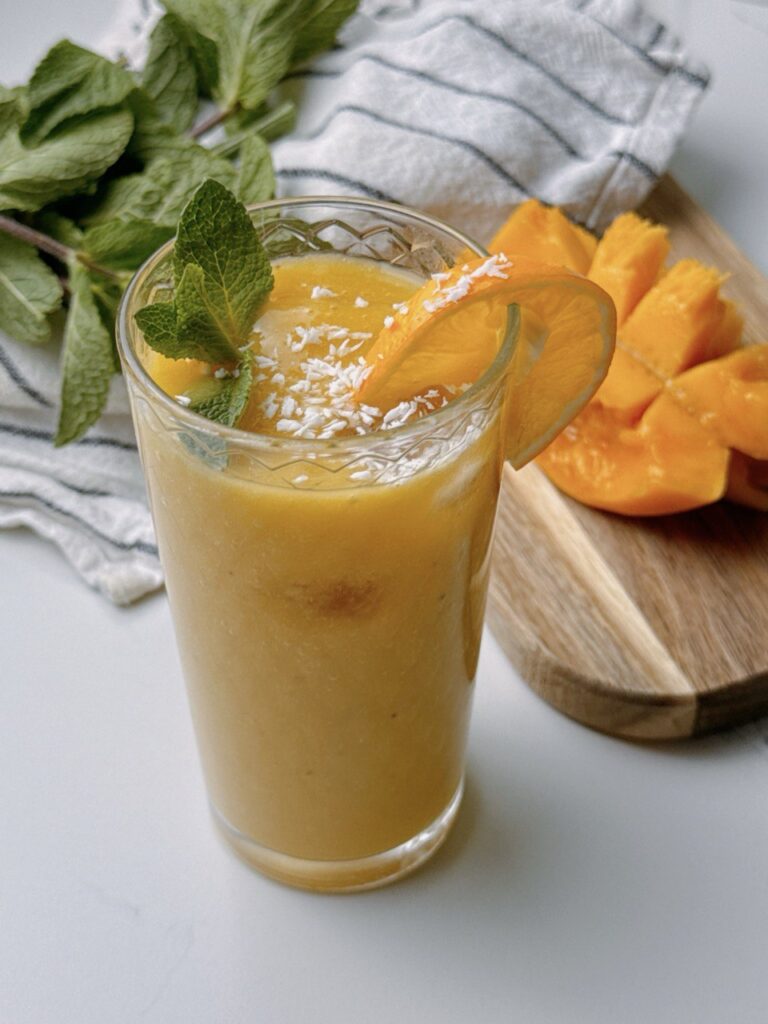 Glass of Mango Banana Ginger Smoothie served with fresh mango in the background