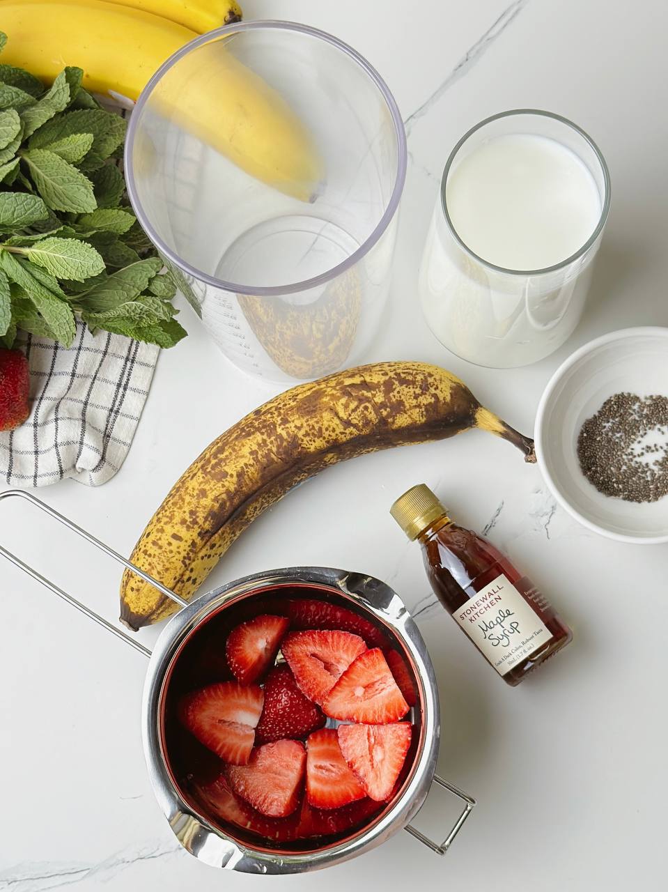 Fresh ingredients for strawberry banana milkshake – banana, strawberries, chia seeds, maple syrup, and milk.